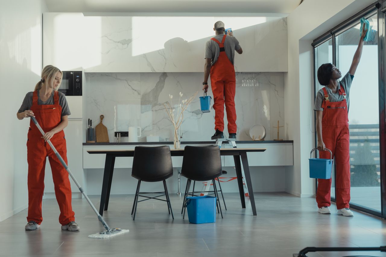 hero-img-01 Group of cleaners in red uniforms mopping and wiping glass in a modern dining room.